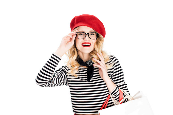 smiling woman in red beret and glasses holding shopping bags isolated on white  - Photo, Image