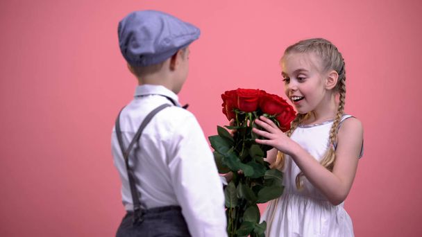 Cute boy in vintage clothes gifting roses to young beautiful girl, first love - Foto, afbeelding