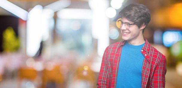 Young handsome student man wearing glasses over isolated background looking away to side with smile on face, natural expression. Laughing confident. - Foto, Bild