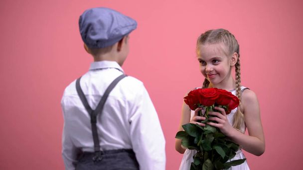 Young gentleman in formal clothes presenting roses bouquet to little female - Foto, afbeelding
