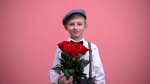 Cute gentleman boy presenting bouquet of red roses into camera, Valentines day - Фото, изображение