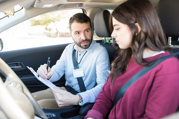 Confident driving examiner showing driving details to learner sitting in car - Foto, Imagen