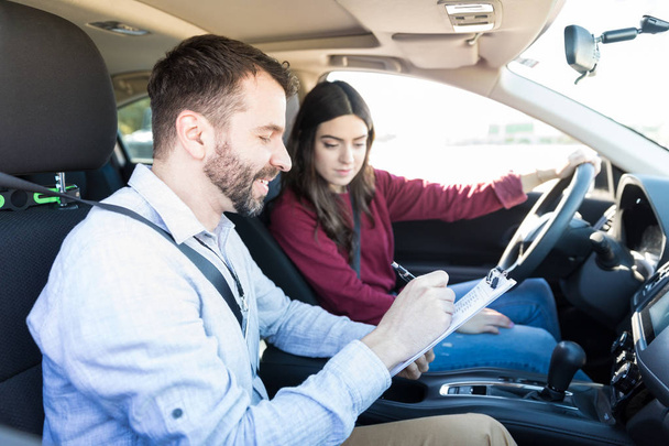 Smiling male examiner writing on clipboard while sitting by new car driver - Photo, Image