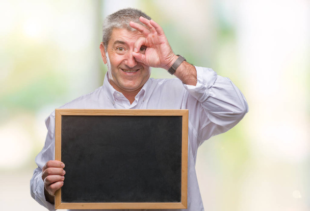 schöner älterer Lehrer Mann hält Tafel über isoliertem Hintergrund mit glücklichem Gesicht lächelnd tut ok Zeichen mit Hand auf Auge durch Finger schauen - Foto, Bild