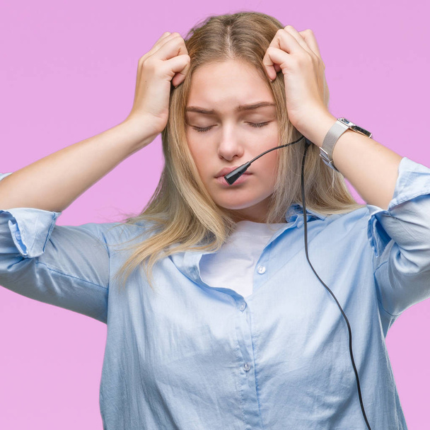 Mujer de negocios caucásica joven que usa auriculares de centro de llamadas sobre un fondo aislado que sufre de dolor de cabeza desesperado y estresado porque el dolor y la migraña. Manos en la cabeza
. - Foto, imagen