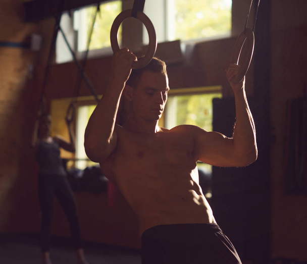 Fit, sporty and athletic sportsman working in a gym. Man training using gymnastic rings. Sports, athletics, lifestyle and fitness concept. - Foto, Imagen