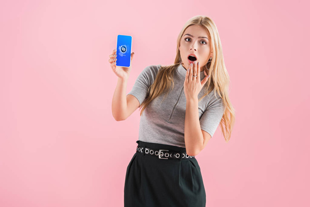 beautiful shocked girl showing smartphone with shazam app on screen, isolated on pink - Photo, Image