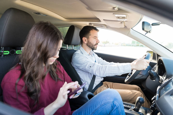 Ισπανόφωνος μέσα του ενήλικα άνδρα οδήγηση ενώ γυναίκα χρησιμοποιώντας το smartphone στο αυτοκίνητο - Φωτογραφία, εικόνα