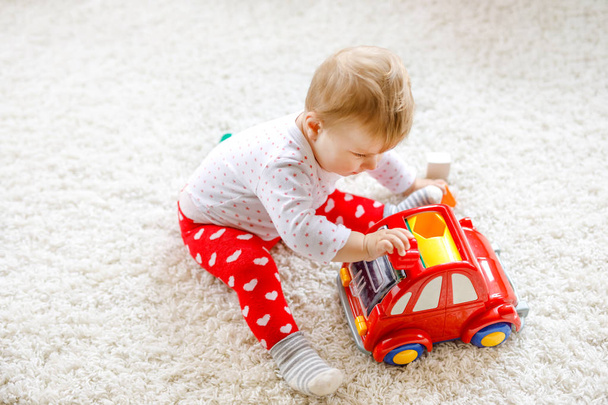 entzückend süße schöne kleine Mädchen spielen mit pädagogischen Holzspielzeug zu Hause oder im Kinderzimmer. gesundes, glückliches Kleinkind mit farbenfrohem roten Auto drinnen. Kinder lernen Farben und Formen. - Foto, Bild