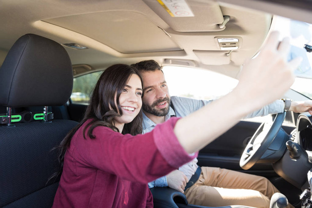 Coppia multietnica sorridente mentre prende selfie con smartphone in auto nuova
 - Foto, immagini