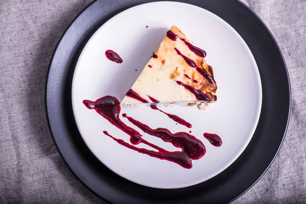 Piece of cheesecake with fruit jam on plate on grey tablecloth - Foto, Imagen