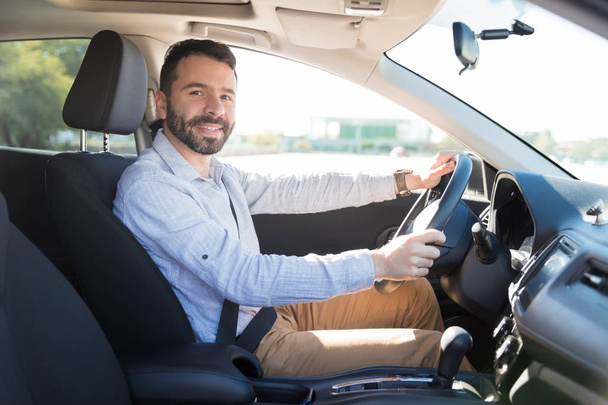 Впевнений серед дорослий власник сидить на водійському сидінні своєї машини і посміхається на камеру
 - Фото, зображення