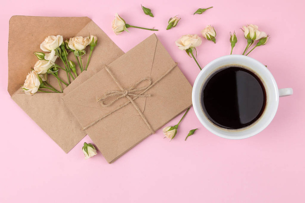 Szép mini rózsák egy csésze kávé és egy borítékot világos rózsaszín háttér. ünnepek. Valentin-nap. nőnap alkalmából. szemközti nézet. - Fotó, kép