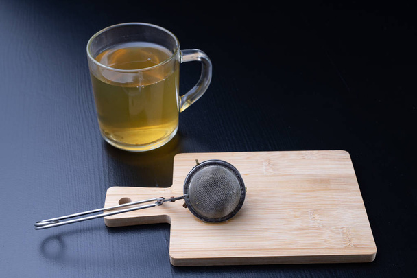 Brewing tea on a black table. Mug with a warm drink. Dark background. - Foto, Imagen