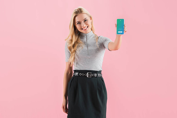beautiful smiling girl showing smartphone with twitter app on screen, isolated on pink - Foto, Bild