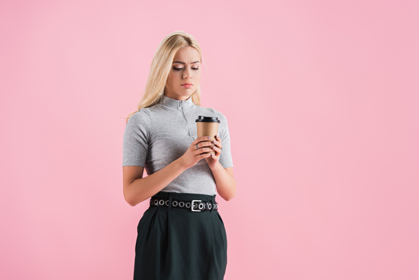 confused blonde girl looking at coffee to go, isolated on pink - Фото, изображение