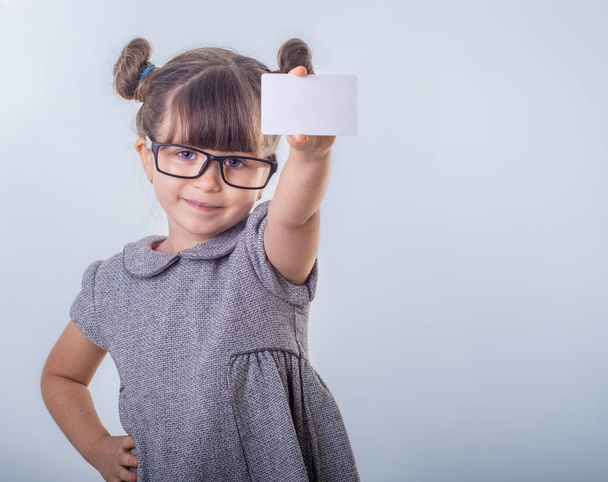 Aranyos mosolygós gyermek szemüveg bankkártya tartja a kezében. Gyerek hitelkártyával. Kis lány mutatja üres üres papír Megjegyzés másol hely. - Fotó, kép