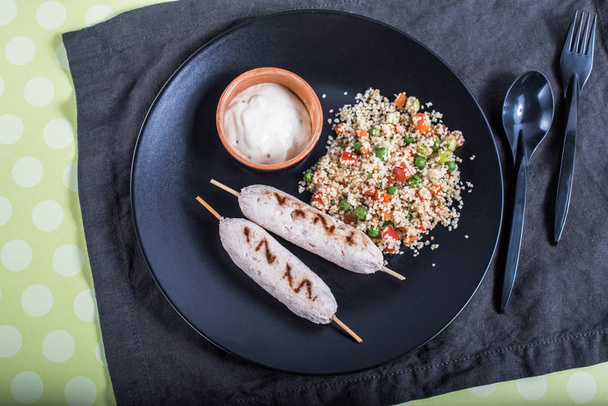 Cuscus with vegetables and grilled sausages on black plate on tablelcoth  - Fotografie, Obrázek