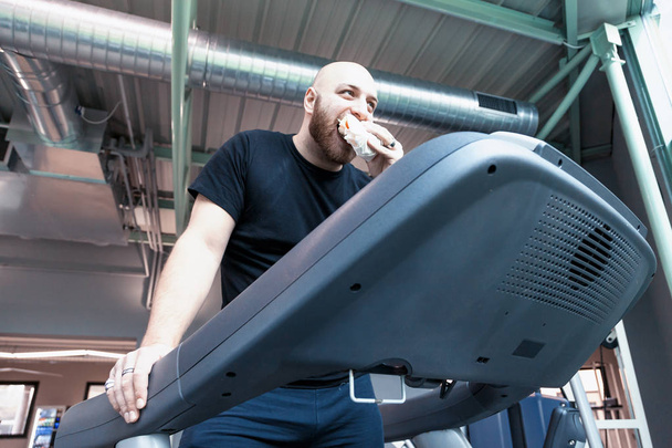 αθλητής δρομέας χαλαρώνοντας τρώει ένα σάντουιτς σχετικά με το οδήγηση μηχανήματα στο γυμναστήριο - Φωτογραφία, εικόνα