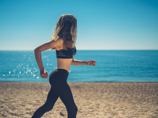 A young woman is exercising and running on the beach in summer - Foto, imagen