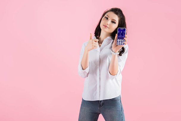 beautiful girl showing thumb up and smartphone with health data on screen, isolated on pink - Photo, Image