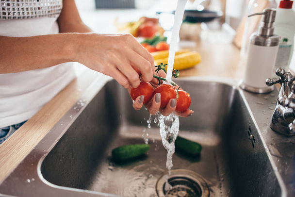 Nainen pesee tomaatteja keittiön pesuallas lähikuva. - Valokuva, kuva