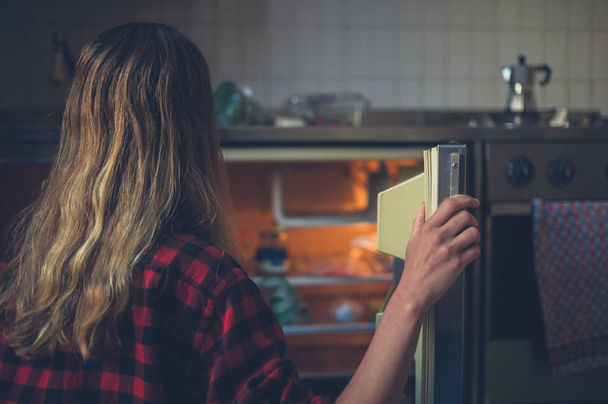 Une jeune femme ouvre la porte de son frigo
 - Photo, image