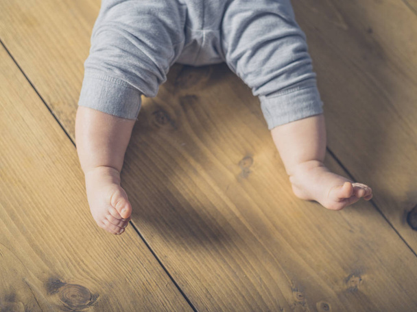 THe legs and feet of a baby lying on the wooden floor - Zdjęcie, obraz