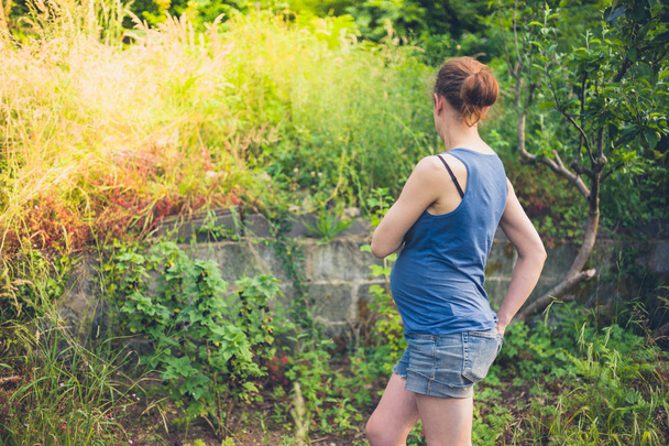 Una joven embarazada está de pie en su jardín en el verano
 - Foto, imagen