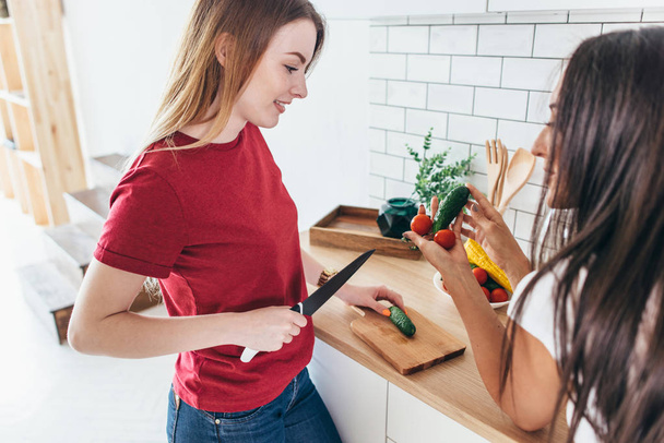 Women preparing food playing with vegetables in kitchen having fun. - Foto, afbeelding