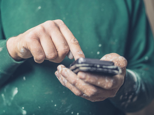 A young man with paint on his hands is using a smartphone - Fotó, kép