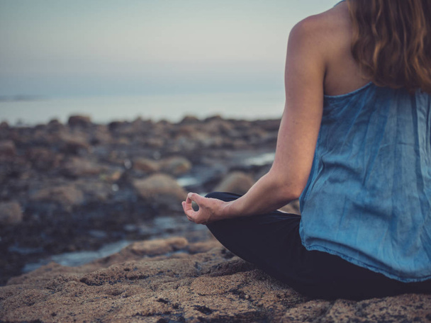 Cropped image of young woman is sitting on the rocks by the sea at sunset meditating - Foto, Imagem