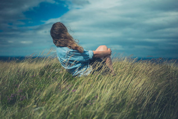 Молодая женщина сидит в поле в ветреный день
 - Фото, изображение