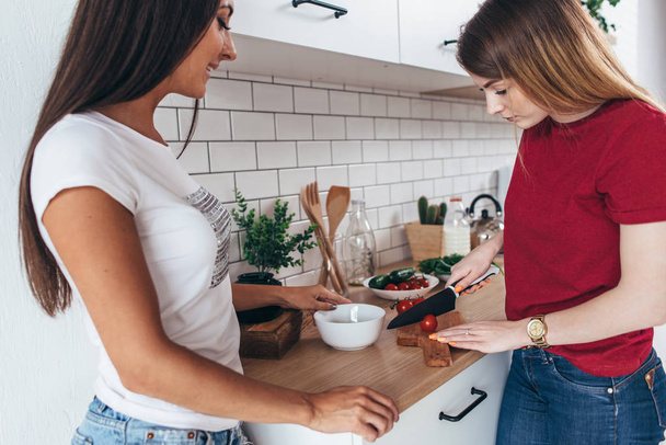 Two girls friends preparing dinner in kitchen cooking salad. - Photo, image