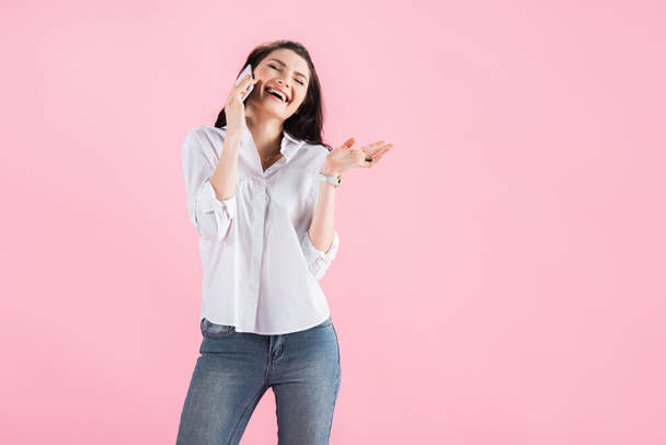 beautiful brunette woman laughing while talking on smartphone, isolated on pink - Photo, Image