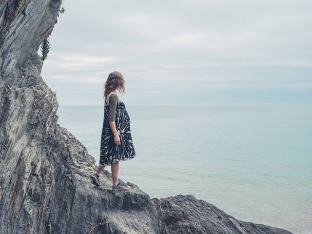 A young woman is standing on some rock on the coast and is looking at the sea - Fotó, kép
