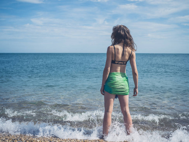 A young woman wearing a bikini and a sarong is standing on the beach - Φωτογραφία, εικόνα