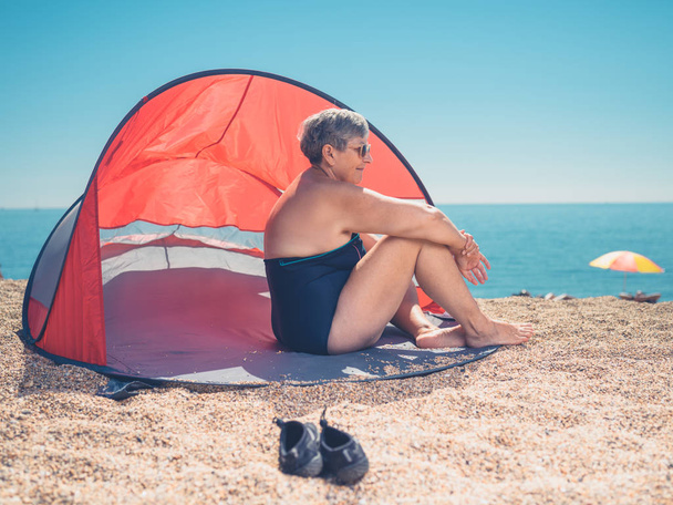 A senior woman is relaxing in a beach shelter - Foto, imagen