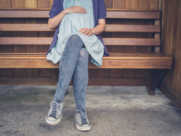 A young pregnant woman is resting on a bench in a shelter - Foto, Imagen