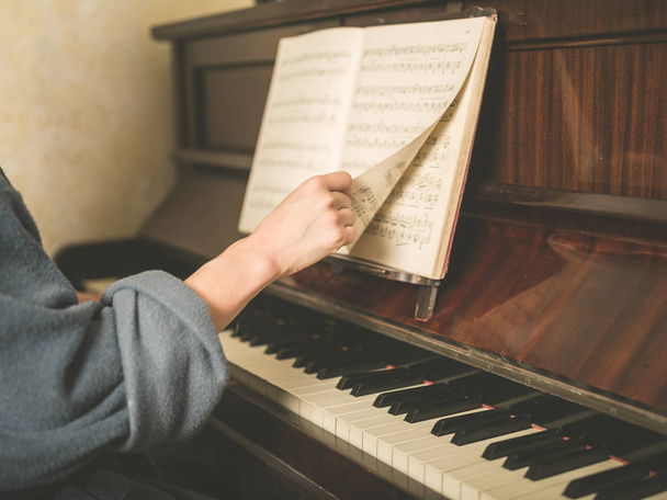 The hand of a young woman is turning music paper at a piano - 写真・画像