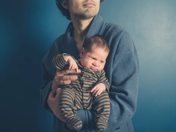 A young father wearing a bathrobe is holding his baby son - Foto, Bild