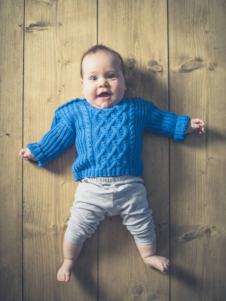 A happy and surprised baby lying on a wooden floor - Fotoğraf, Görsel