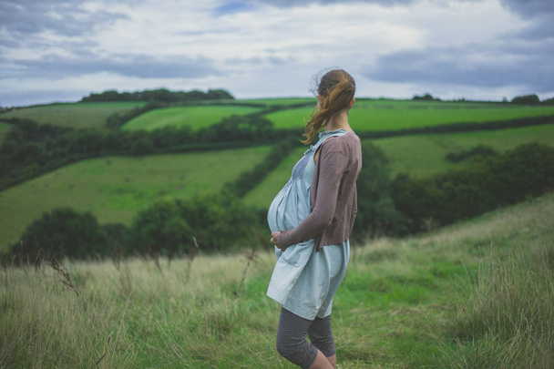 Молодая беременная женщина стоит в сельской местности, держа своего ребенка шишку
 - Фото, изображение
