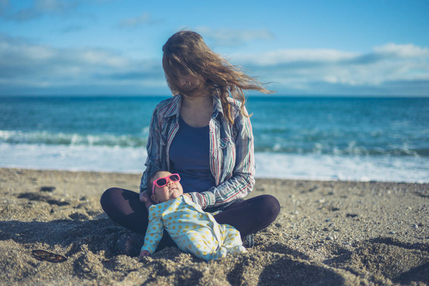 A cool baby is wearing sunglasses and is chilling out on the beach with his mother - Foto, Imagem