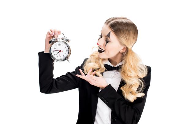 cheerful female clown looking at alarm clock isolated on white  - Φωτογραφία, εικόνα