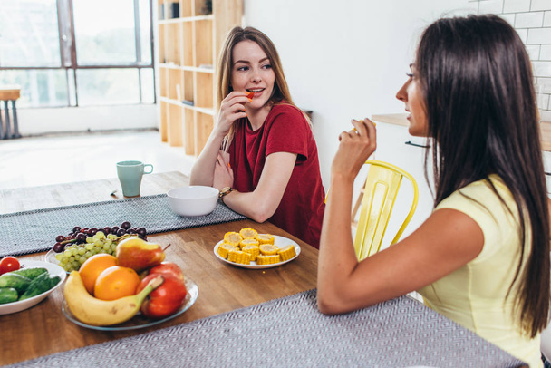 Γυναίκες φίλους έχοντας φρούτα στο πρωινό στην κουζίνα. - Φωτογραφία, εικόνα