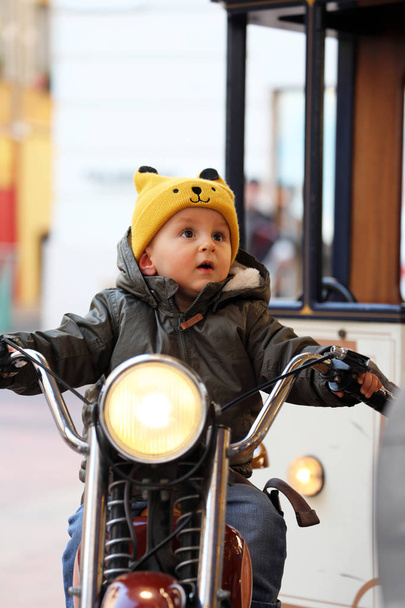 Милий хлопчик, сидячи на Vintage мотоцикл, маленький хлопчик сміятися на каруселі, крупним планом портрет - Фото, зображення