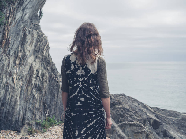 Una joven está de pie sobre una roca en la costa y está mirando al mar
 - Foto, imagen