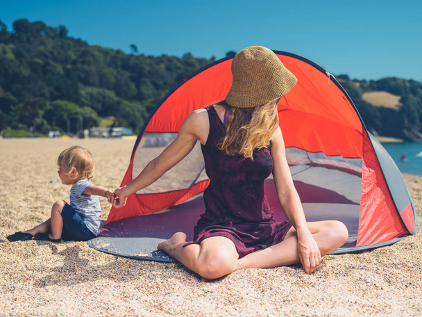 A young mother is relaxing in a beach shelter with her toddler - Foto, imagen