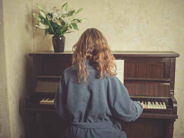 A young woman in a bathrobe is playing the piano - Foto, Imagen
